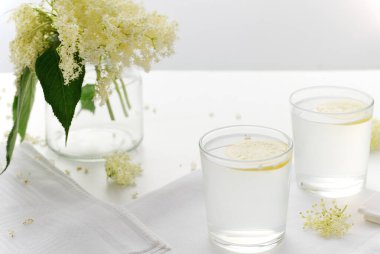 Beyaz arka planda limon dilimleri olan bir bardak Elderflower limonatası. Alternatif tıp. Çiçek, çiçek. Seçmeli odak, yatay yönelim.