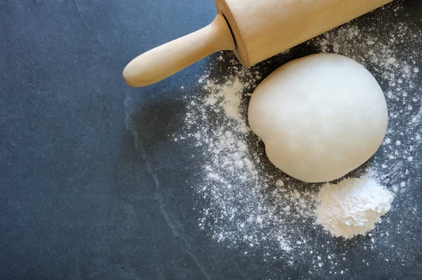 Ball of dough with rolling pin for dumplings or pasta  on the stone board. Dough with flour, eggs, salt. Raw dough.Homemade baking.