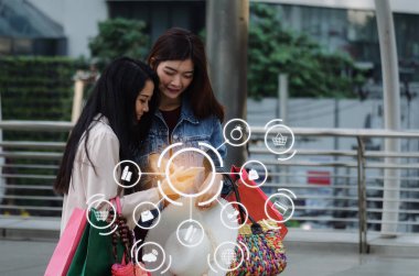 Özel Fırsat içinde hareket eden telefon izliyor ve simge ürün diyagramı, teknoloji, yaz satış, ödeme ve alışveriş online kavramı ile büyük şehirde alışveriş çantası elinde iki güzel Asyalı Genç kadın