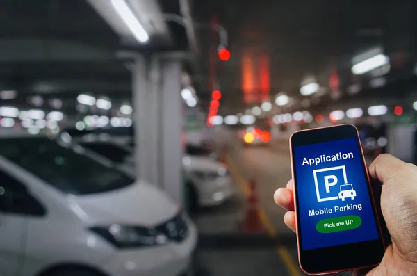 pick me up, mobile smart phone in hand using application for intelligent car park on blurred parking car indoor background,  mobile auto parking, online technology and internet connection concept