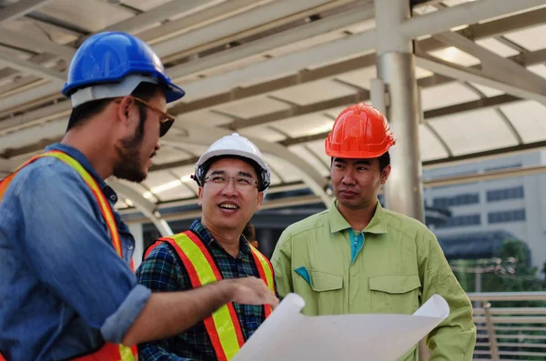 工程师 技术员和建筑师小组在现代城市建筑背景 建筑工地 工业和工人概念上制定蓝图规划与安全头盔计划 — 图库照片