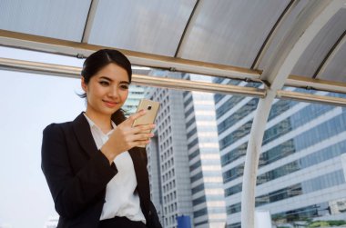 Şehir arka plan, ağ teknolojisi, internet ve dijital kavramı binada cep telefonu ile sosyal ağ oyun modern siyah takım elbise giyen güzel gülümseyen genç Asya iş kadın