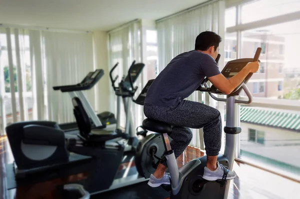 muscular young asian man exercising his legs cardio training on bicycle in fitness gym for good healthy at the morning, bodybuilder, lifestyle, exercise fitness, workout and sport training concept