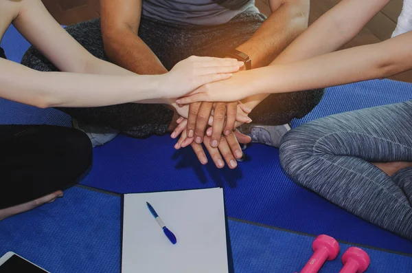 close up of sport people team planning to reach their goal and doing high five together sitting on yoga mat in fitness gym, exercise, training, workout, partnership, success and teamwork concept