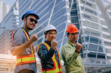 yeah, finally we did it, group of engineer, technician and architect screaming showing their strong hands together standing in modern city building background, construction site and industry concept