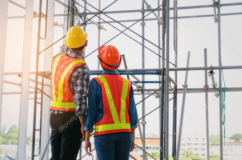 couple of engineer or technician man and woman with safety helmet holding mobile radio phone planning about building plan to greeting start up project in construction site building, industry concept