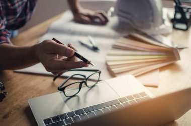 kavram Mühendislik İnşaat sahasında yeni proje için planya tartışılması sırasında beyaz emniyet kask, plan ve renk paleti üstünde okul sırası ile dizüstü bilgisayar üzerinde kalemle işaret Proje Yöneticisi