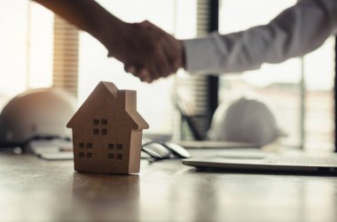 İnşaat işçisi iş Toplantı bittikten sonra müşteri ile tokalaşırken ofis merkezi ev modeli, ev kredisi sözleşmesi kavramı arkasında inşaat sahasında sözleşmede proje başlatmak için