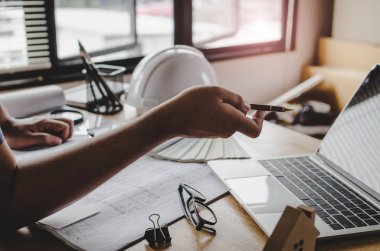 kavram Mühendislik İnşaat sahasında yeni proje için planya tartışılması sırasında beyaz emniyet kask, plan ve renk paleti üstünde okul sırası ile dizüstü bilgisayar üzerinde kalemle işaret Proje Yöneticisi