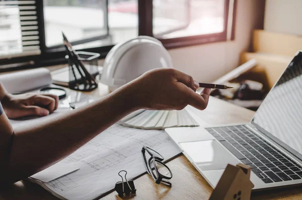 kavram Mühendislik İnşaat sahasında yeni proje için planya tartışılması sırasında beyaz emniyet kask, plan ve renk paleti üstünde okul sırası ile dizüstü bilgisayar üzerinde kalemle işaret Proje Yöneticisi