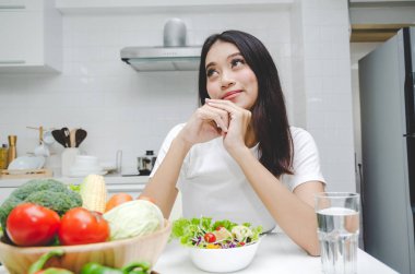 güzel genç Asyalı kadın ince vücut diyet ve beslenme beyaz gömlekli sağlıklı gıda, oturma mutfak iç içinde ev, yaşam tarzı, sağlıklı, iyi taze sebze salatası diyet yiyecek ve içecek konsepti