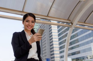 Şehir arka plan, ağ teknolojisi, internet ve dijital kavramı binada cep telefonu ile sosyal ağ oyun modern siyah takım elbise giyen güzel gülümseyen genç Asya iş kadın