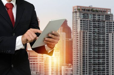 gün doğumu ve Cityscape arka plan sırasında mobil tablet ile finans haberleri hakkında bilgi okuma uygun genç yakışıklı iş adamı, ağ teknolojisi, finans yatırımı, ortaklık kavramı