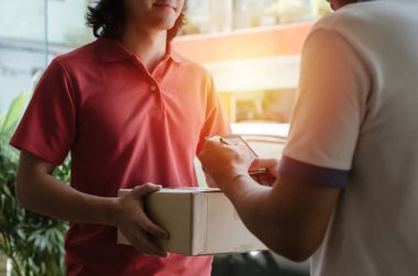 evde kırmızı üniformalı gülen yüz yüze gelen ev teslim servisi ile kuryeden koli posta kutusu alan dijital cep telefonuna imza atan genç adam, ekspres teslimat konsepti