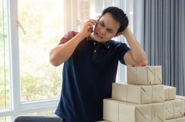 Kobi. Depresif. genç asyalı adam ciddi masada cep telefonu ve teslimat ambalaj kutusu ile konuşurken, küçük işletme sahibi evde çalışan, işletme sahibi, başlangıç ve alışveriş online kavram