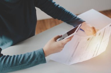 evde masa üzerinde aile bütçesi maliyet faturaları ile online ödeme, plan para maliyet tasarrufu, yatırım, iş finansmanı ve giderleri kavramı ile online arama ve ödeme için cep telefonu kullanarak genç kadın el