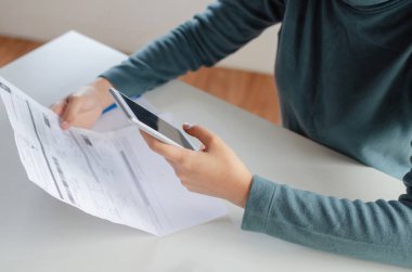evde masa üzerinde aile bütçesi maliyet faturaları ile online ödeme, plan para maliyet tasarrufu, yatırım, iş finansmanı, giderleri kavramı ile online arama ve ödeme için cep telefonu kullanarak genç kadın elleri