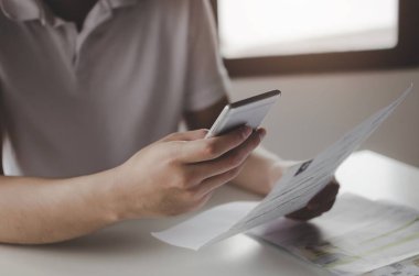 evde masa üzerinde aile bütçesi maliyet faturaları ile online ödeme ve taramak için cep telefonu kullanarak genç adam elleri, plan para maliyet tasarrufu, yatırım, iş finansmanı, giderleri kavramı