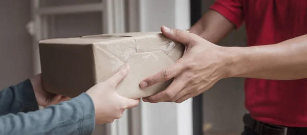 Panoramic banner. delivery service man in red uniform with woman customer receiving parcel post box from courier at home, cargo shipping, express delivery service, online shopping and logistic concept