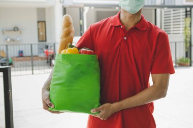 Kapıdaki müşteriler için taze yiyecek çantası, market, sağlıklı yiyecek, ekspres dağıtım, yemek teslimatı, online alışveriş konsepti taşıyan mavi üniformalı bir teslimatçı.