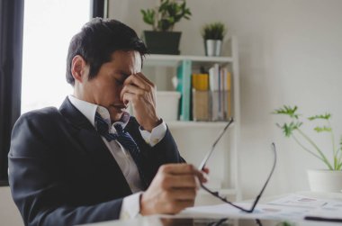 yorgun Asyalı genç işadamı stresli hissediyor ve gözlük çıkartıyor bilgisayar, aşırı çalışma, ofis sendromu, iş sorunu ve finansal konsept üzerinde uzun süre çalıştıktan sonra göz yorgunluğu hissediyor