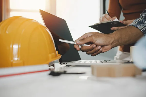 hands of group engineer and architect working on laptop computer and blueprint on workplace desk in meeting room project at construction site office, contractor, engineering and construction concept