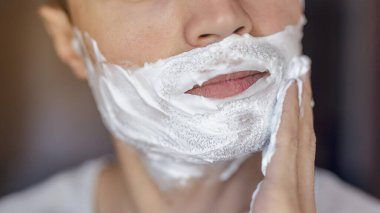 Genç adam traş olur, yüzünde köpükle jilet izi olur.