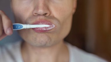 Beyaz tişörtlü genç adam dişlerini fırçalıyor.