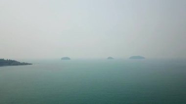 Tayland denizi üzerinde sis. Küçük adalar uzaktan görülebilir ve gökyüzü beyaz bir duman tabakasıyla kaplıdır. Küçük dalgalı yeşil su. Kamboçya 'dan duman geliyor. İHA ateşleniyor