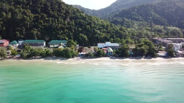 Die grünen Hügel der Insel sind mit Palmen bedeckt, der Himmel ist bewölkt und ein Sonnenstrahl bricht durch. Klares türkisfarbenes Wasser am Strand mit goldenem Sand. Die Leute entspannen sich. Drohne. — Stockvideo