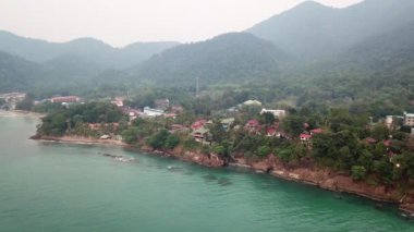 Yeşil Chang adası Kamboçya 'daki bir yangından dolayı dumanla kaplandı. Yeşil ağaçlar, palmiye ağaçları ve tepeler sis bulutlarıyla kaplıdır. Oteller denizin önündeki bir uçurumun üzerinde duruyor. Turkuaz su.