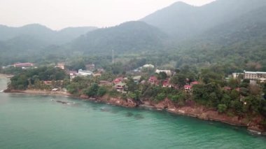 Yeşil Chang adası Kamboçya 'daki bir yangından dolayı dumanla kaplandı. Yeşil ağaçlar, palmiye ağaçları ve tepeler sis bulutlarıyla kaplıdır. Oteller denizin önündeki bir uçurumun üzerinde duruyor. Turkuaz su.