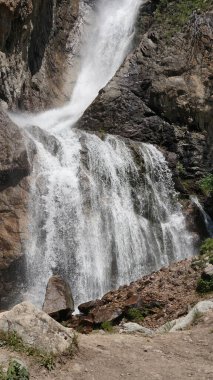 Dik kayalıklardan aşağı doğru akan dramatik şelale beyaz su püskürtüyor. Doğal dağ manzarası, taştan oluşumlara karşı akan suyun ham gücünü gösteriyor.