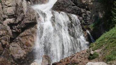Artan saf beyaz su engebeli granit kayalıklardan aşağı akıyor, yoğun bitki örtüsüyle çevrili, saf güzellik ve gücü ön plana çıkarıyor.