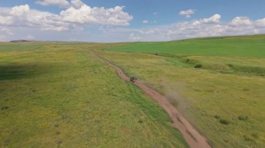 Black pickup truck driving across vast green meadows, kicking up dust trail under cloudy summer sky, revealing expansive countryside landscape and sense of freedom and adventure