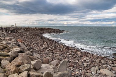 Faks Koyu 'nun Rocky sahili, arka planda deniz feneri. Seltjarnarnes, Reykjavik, İzlanda.
