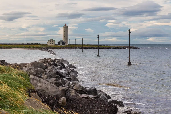 Faks Koyu 'nun Rocky sahili, arka planda deniz feneri. Seltjarnarnes, Reykjavik, İzlanda.