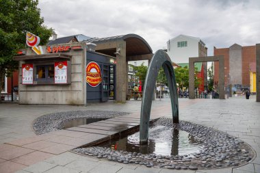 Reykjavik, İzlanda - 27 Ağustos 2015: Başkent merkezindeki kemer şekilli çeşme. Arka planda sosisli ve buzlu restoran..