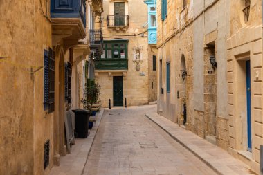 Birgu, Malta - 26 Haziran 2021: Eski kasabanın renkli balkonları ve geleneksel kapılarıyla sessiz dar bir taş sokak.