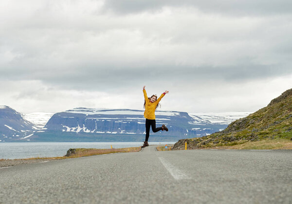 Running girl in a yellow raincoat on a road in Iceland