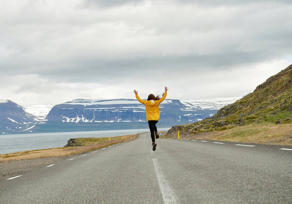 Running girl in a yellow raincoat on a road in Iceland