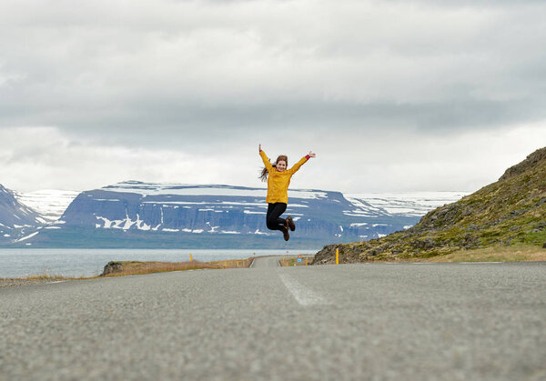 Beautiful girl in a yellow raincoat jumping on the autobahn in Iceland