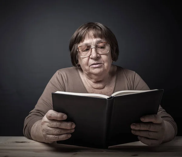 Uma Mulher Idosa Óculos Senta Mesa Livro Tonificado — Fotografia de Stock