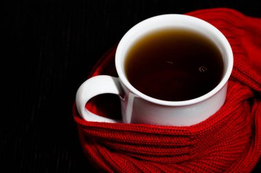 Koyu arka plan üzerinde çay ve sıcak örme eşarp ile beyaz kupa.