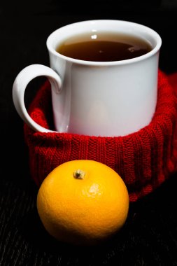 Beyaz kupa ile çay ve sıcak örme eşarp koyu arka plan üzerinde. Tonda.