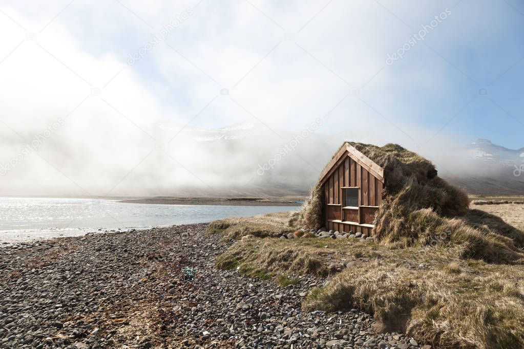 Small wooden house with grass roof in the Iceland fjord