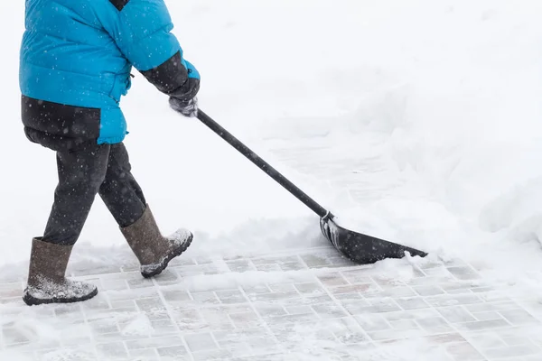 穿着温暖的蓝色夹克的老妇人用雪清除雪飘，雪飘飘 — 图库照片