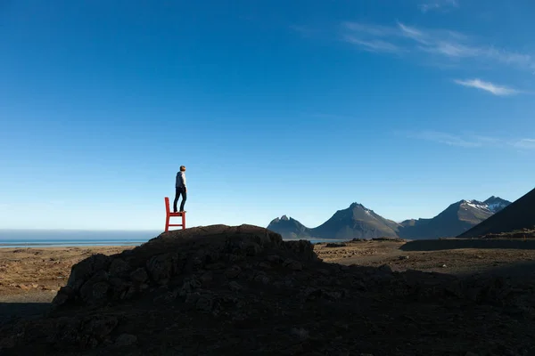 Girl on a red wooden chair on a empty stony landscape in Iceland — Stock Photo, Image
