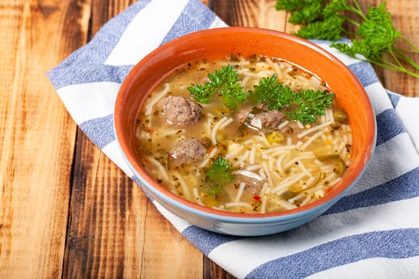 Homemade soup with noodles and meatballs on a wooden table. Trad