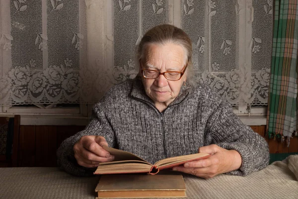 Elderly woman reads book in rustic interior — Stock Photo, Image